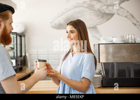 Caffè il concetto di Business - giovani smart barbuto barista godere di parlare e dare portar via tazza di caffè per piuttosto cliente. Foto Stock