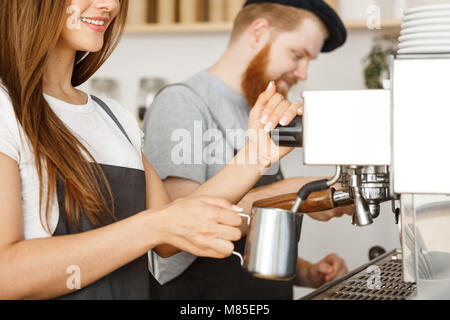 Caffè il concetto di Business - Ritratto di signora barista grembiule in preparazione per la cottura a vapore e il latte per il caffè ordine con il suo partner in piedi presso il cafe. Foto Stock