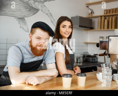 Caffè il concetto di Business - Positivo giovane uomo barbuto e bella attraente dama barista giovane nel grembiule guardando la fotocamera mentre in piedi al bancone bar Foto Stock