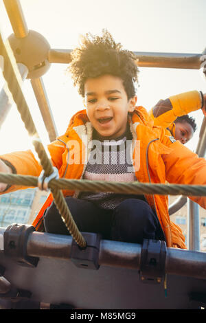 Dei bambini felici di arrampicata in un parco giochi urbano la costruzione in una giornata di sole Foto Stock