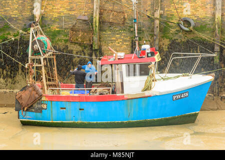 Due pescatori che lavorano sul ponte di una barca da pesca nel porto di whitstable kent, con la bassa marea. Foto Stock