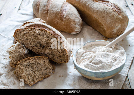 Tutto il pane di grano e farina su sfondo chiaro. Vaso in ceramica piena di farina integrale Foto Stock
