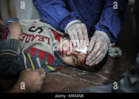 Provincia Ghouta, Siria. Il 15 marzo, 2018. Un ragazzo siriano riceve il primo soccorso in un ospedale di fortuna dopo che egli è stato ferito nel corso di attacchi aerei dalle forze fedeli al presidente siriano Assad in Kafr Batna, un sobborgo esterno a Damasco in Siria orientale della provincia Al-Ghouta, 15 marzo 2018. Foto: Anas Alkharboutli/dpa Credito: dpa picture alliance/Alamy Live News Foto Stock