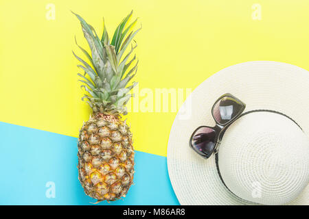 Di ananas maturo donna di cappello di paglia Occhiali da sole a dividere le due tonalità giallo blu sullo sfondo. Estate Vacanze viaggi Frutti Tropicali Fashion Concept. Lay piatto Foto Stock