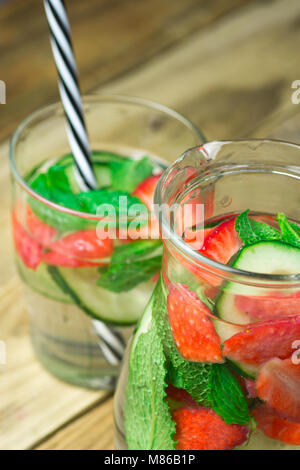 Il vetro e la brocca con fresco fresco infuso Detox acqua con maturi organici di fragole a fette cetrioli menta. Plank Sfondo legno. Bibita salutare Detox Foto Stock