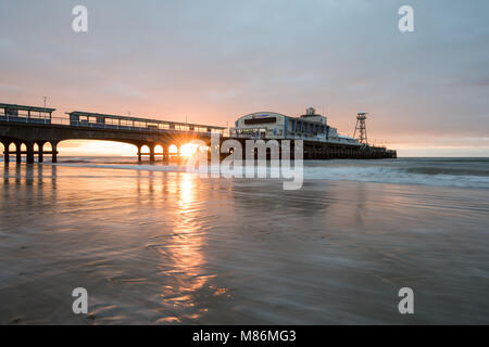 Inverno il sole sorgere dietro il molo di Bournemouth nel Dorset fotografata dalla spiaggia Foto Stock