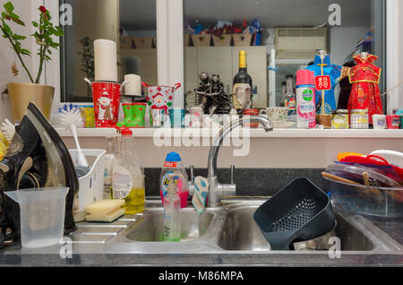 Un lavello da cucina ingombra di lavaggio fino, un ferro da stiro, materiali per la pulizia. Foto Stock