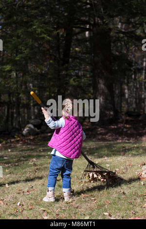 Il Toddler girl learning per rastrellare foglie su un freddo giorno di autunno nel Maine Foto Stock