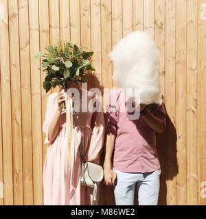 Sposa e lo sposo holding caramella di cotone e fiori nella parte anteriore delle loro facce Foto Stock