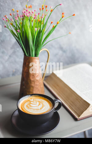 Una tazza di caffè ' latte art ' con la sveglia e il libro aperto sul tavolo Foto Stock