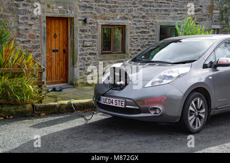 Una Nissan Leaf auto elettrica essendo addebitato al di fuori di un cottage, Newton, Clitheroe, Lancashire, Regno Unito. Foto Stock