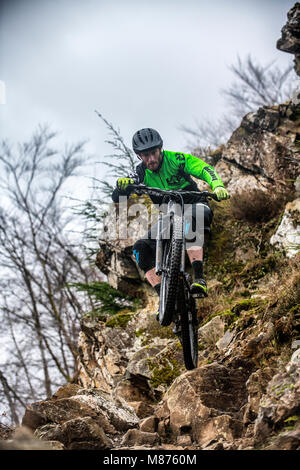 Un mountain biker cavalca un sentiero roccioso a Coed-y-Brenin in Snowdonia, il Galles del Nord. Foto Stock