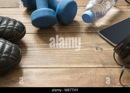 Sport e fitness equipmen con le scarpe da ginnastica, manubri, asciugamano e cuffie sul pannello di legno. Vista da sopra con lo spazio per il tuo testo. Foto Stock