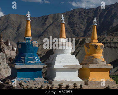 Tre stupa buddisti di blu, bianco e giallo con giallo spiers contro lo sfondo di una enorme montagna. Foto Stock