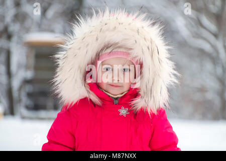 Poco carino ragazza in un grande pellicce cofano in inverno Foto Stock