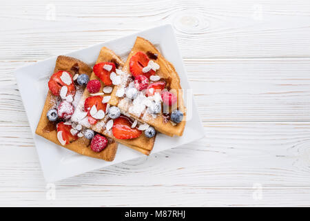 Crespelle con fragole, mirtilli, mandorla e salsa al cioccolato bianco su sfondo di legno. Vista dall'alto. Spazio di copia Foto Stock