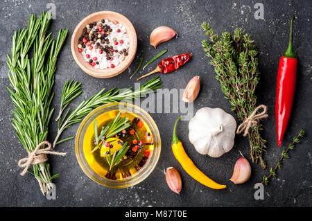 Erbe e spezie. Rosmarino, timo, peperoncino, aglio, olio d'oliva, sale e pepe sul tavolo scuro. Gli ingredienti della cucina. Vista superiore Foto Stock