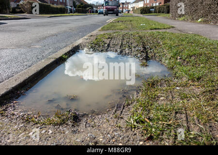 Una grande pozza di fango sul lato di una strada dove un'erba orlo dovrebbe essere. Questo è causato dalle automobili parcheggio sull orlo quando è umido. Foto Stock