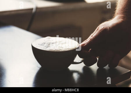 Vista ravvicinata della mano di un uomo che lavora in una casa di caffè la preparazione di caffè espresso in attesa per la macchina da caffè per terminare versando la beve fresco Foto Stock