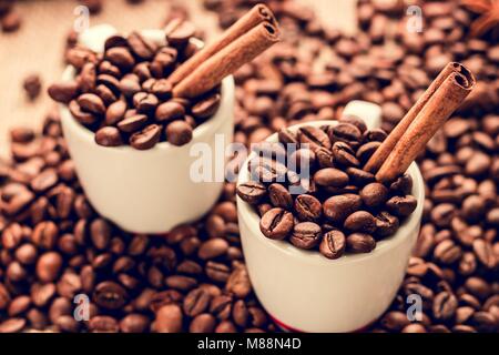 Bianco tazze di espresso con i chicchi di caffè e bastoncini di cannella Foto Stock