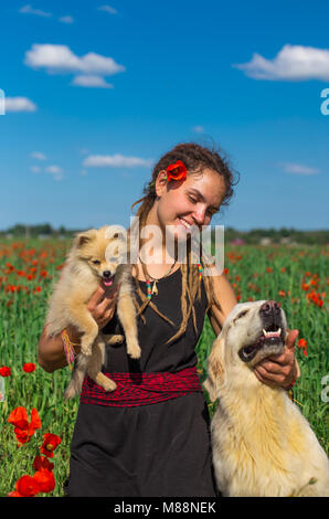 Ragazza con dreadlocks è a piedi con due splendidi cani nel campo di papavero. Regione di Almaty, Kazakhstan. Foto Stock