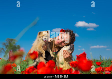 Ragazza con dreadlocks è a piedi con due splendidi cani nel campo di papavero. Regione di Almaty, Kazakhstan. Foto Stock