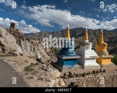 Tre luminose stupa buddisti sono blu, bianco e giallo su una montagna alta strada che porta alle rovine del monastero tibetano. Foto Stock