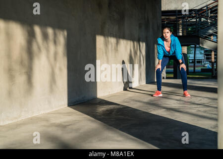 Femminile prendendo una pausa in piedi piegati e cattura il suo respiro dopo l'esecuzione di un allenamento in città. Foto Stock