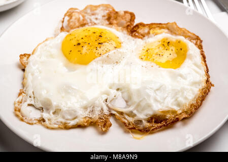 Tradizionale colazione israeliana con due uova fritte, formaggio giallo, insalata, un rotolo di fresco e una tazza di cappuccino. Primo piano sulle uova fritte Foto Stock