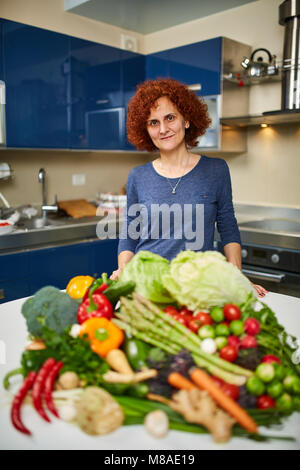 Donna cottura a casa, avente un grande mucchio di verdure su scheda Foto Stock