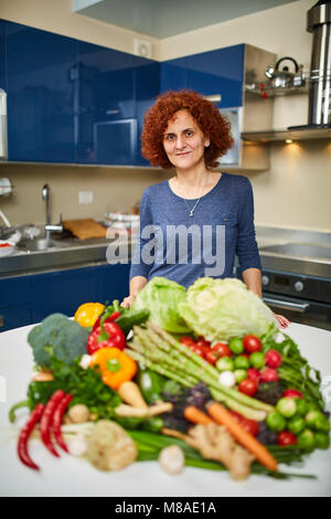 Donna cottura a casa, avente un grande mucchio di verdure su scheda Foto Stock