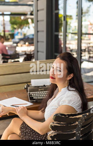 La scrittura e il concetto di freelance. Scrittore femmina che indossa una camicia bianca e la polka dot mantello in outdoor cafe con retro nastri inchiostratori per macchine da scrivere su un tavolo di legno. Copia spac Foto Stock