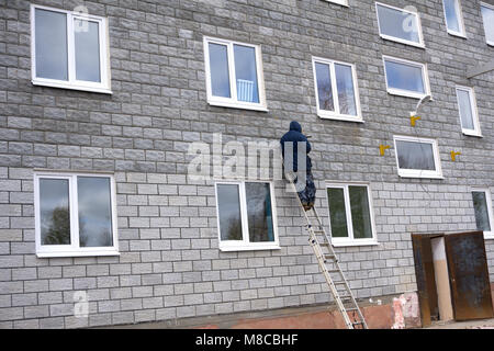 Sorridente operaio edile sulla scaletta sotto il tetto della casa Foto Stock