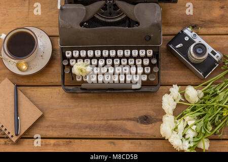 Scrittore flatlay. Grigio scuro retrò i nastri inchiostratori per macchine da scrivere con il blocco note e penna nera, una tazza di caffè nero, vintage fotocamera a pellicola bianco e ranunculus su backgrou in legno Foto Stock