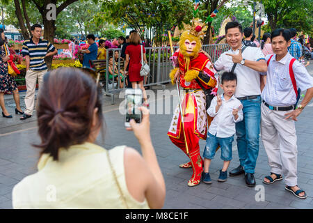 Un gruppo di persone che hanno una fotografia scattata con un uomo in un tradizionale costume di scimmia, Ho Chi Minh City, a Saigon, Vietnam Foto Stock