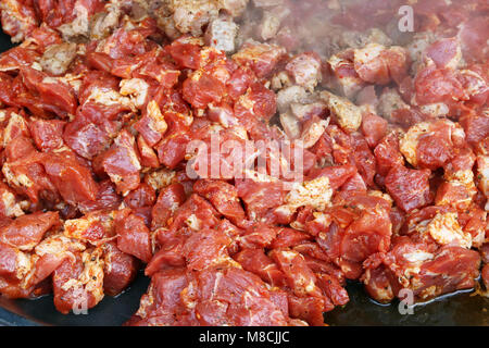 Pezzi di carne di maiale in rosso salsa chili vengono fritte in padella. Street food concept. Molla di colpo all'aperto Foto Stock