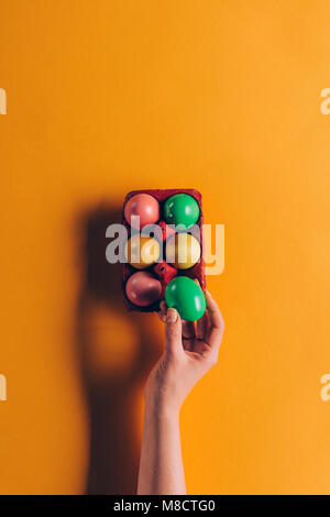Immagine ritagliata della donna prendendo verde uovo di pasqua dal vassoio delle uova su Orange Foto Stock