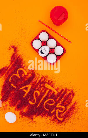 Vista superiore del segno di pasqua fatta di sabbia rossa con uova di gallina con smiley su Orange Foto Stock