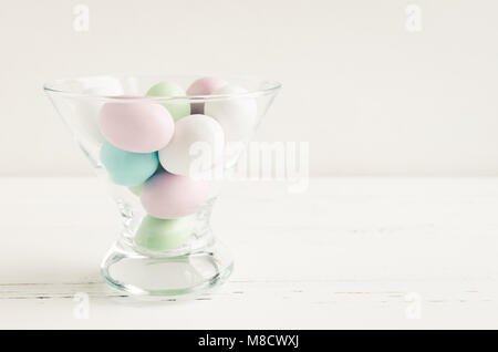 Composizione di pasqua con uova di cioccolato in colori pastello in recipiente di vetro su bianco shabby chic sfondo di legno con posto per il testo. Felici vacanze di Pasqua Foto Stock