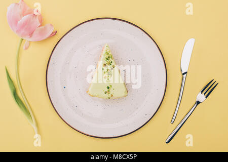 Vista superiore del pezzo di torta sulla piastra, tulip flower e posate isolato su giallo Foto Stock