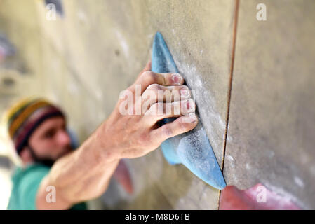 Scalatore bouldering in una sala sportiva - Tenere il manico di una artificiale parete di roccia Foto Stock