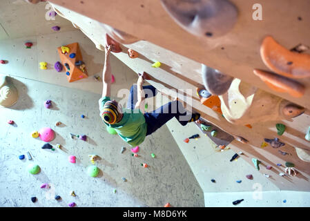 Scalatore bouldering in una sala sportiva - Tenere il manico di una artificiale parete di roccia Foto Stock