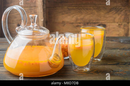 Bacche di olivello spinoso tè in una teiera trasparente con miele sul tavolo di legno. Tradizionale autunno bevanda. Stile rustico. Messa a fuoco selettiva Foto Stock