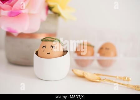 Uova di pelo. Concetto di pasqua. Uova dipinte con gli occhi e la bocca. Ragazza di uovo in bianco stand. Fiori, rose Foto Stock