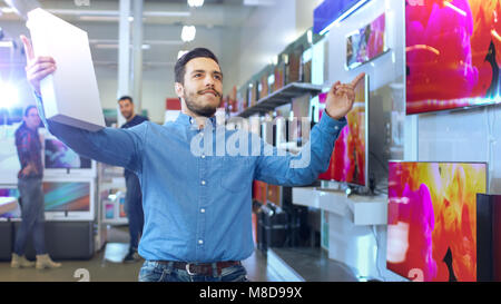 Giovane uomo nel negozio di elettronica ha acquistato il modello più recente del Tablet PC e danze felicemente con la casella. Luminose e moderne Store Foto Stock