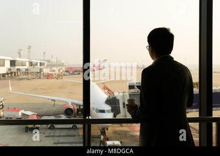 Giovane imprenditore stand presso il terminal in aeroporto internatianal durante il tramonto e chiacchierare al telefono per informarli della loro importante business travel Foto Stock