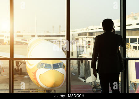 Giovane imprenditore stand presso il terminal in aeroporto internatianal durante il tramonto e parlare al telefono per informarli del loro importante business travel Foto Stock