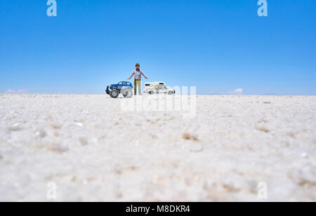 Falsa immagine in prospettiva del ragazzo e toy carrello su saline, in piedi alti più di veicolo in background, Salar de Uyuni, Bolivia Foto Stock