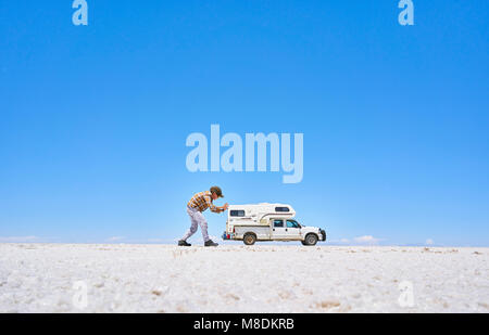 Falsa immagine in prospettiva del ragazzo sul sale appartamenti, fingendo di spingere il veicolo, veicolo in background, Salar de Uyuni, Oruro, Bolivia Foto Stock