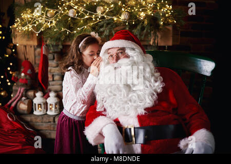 Ragazza giovane visitare Santa, whispering in Santa l orecchio Foto Stock